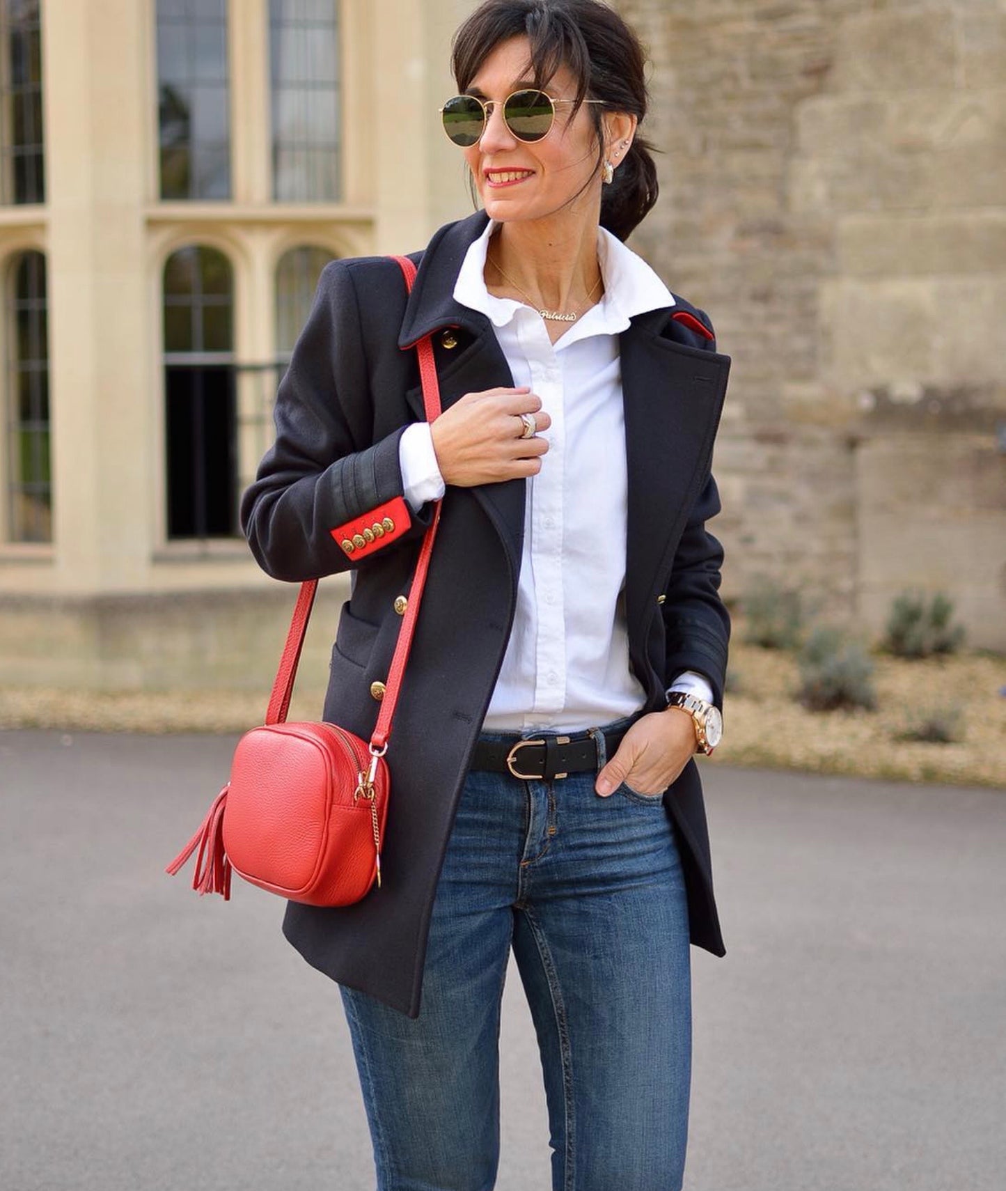 An image of a woman in a white shirt, navy blazer and jeans carrying a red leather messenger bag